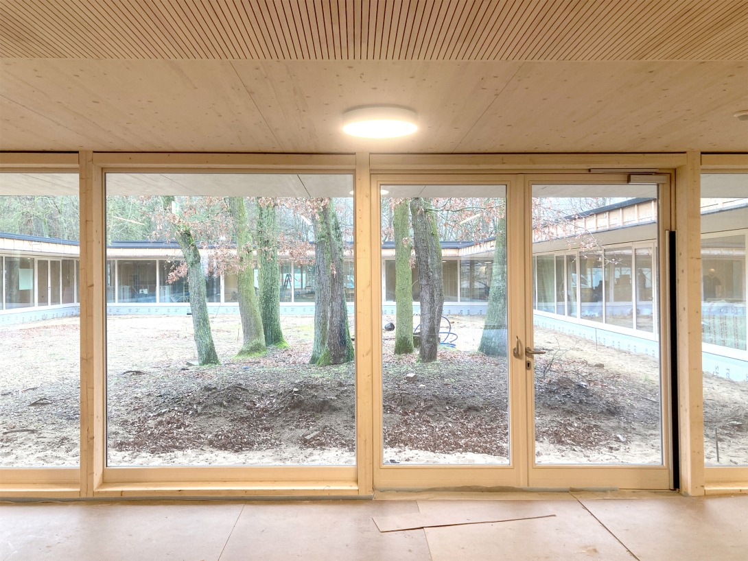 Blick durch ein bodentiefes Holzfenster in den innenliegenden Hof
